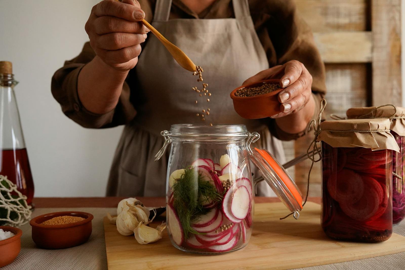 Close-up of hands preparing homemade pickles with spices in a rustic kitchen setting.